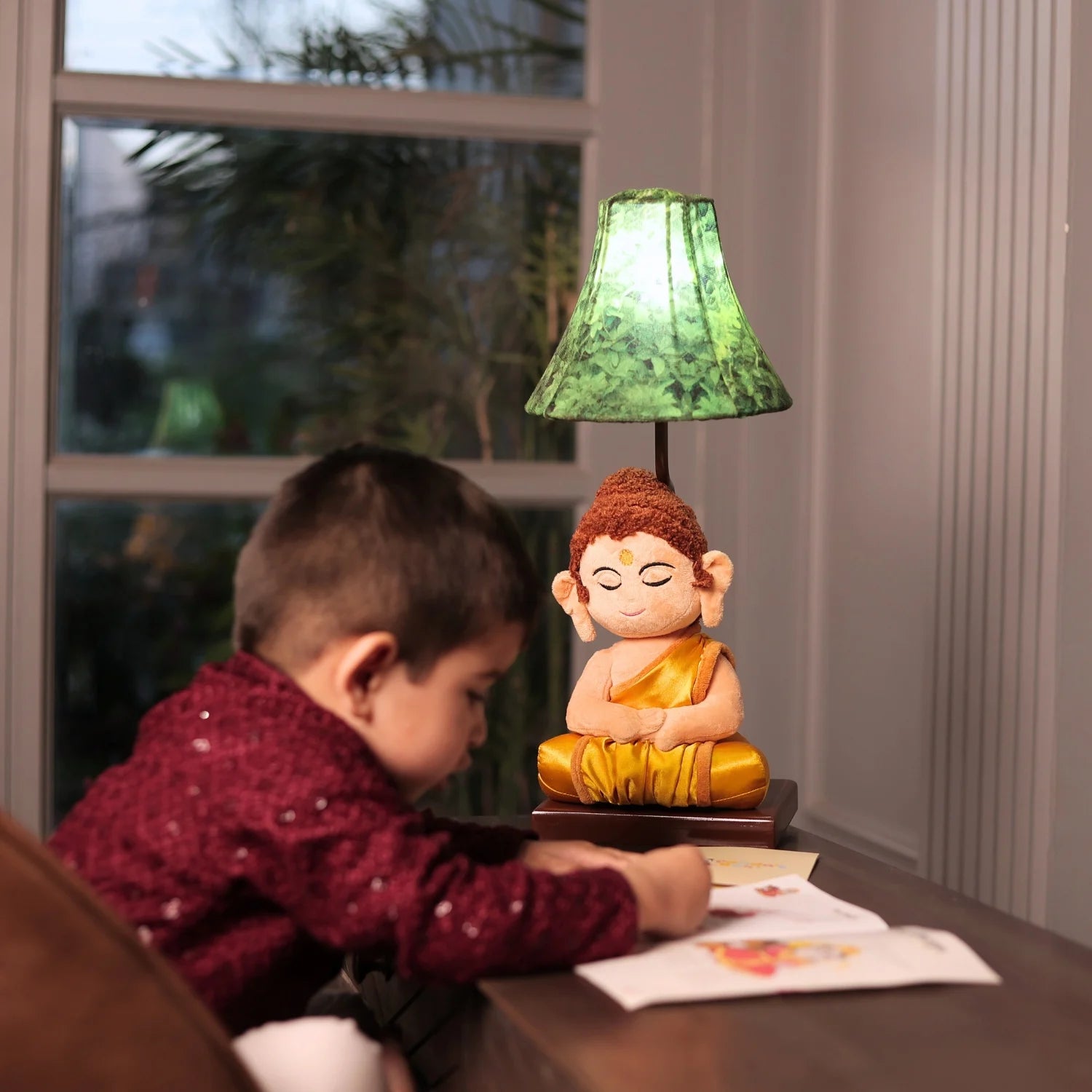 Child sitting at a table with a small Buddha statue lamp in the background